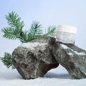 Visuel de la crème Belle en Hiver Bénédicte photographiés sur de la roche avec des branches de sapin, de la neige sur un fond bleu