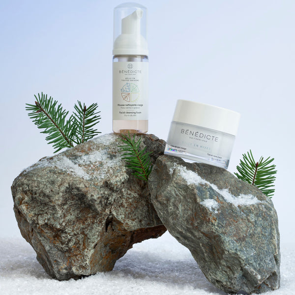 Visuel de la crème Belle en Hiver et de la mousse nettoyante photographiés sur de la roche avec des branches de sapin et de la neige sur fond blanc